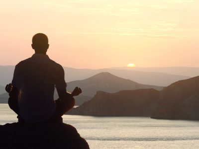 Silhouette of a man meditating yoga at dawn in a lotus position by the sea