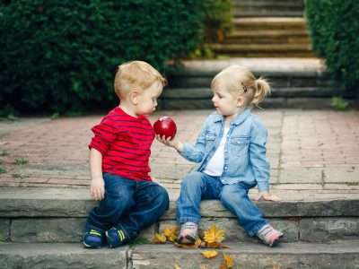 Group portrait of two white Caucasian cute adorable funny children toddlers sitting together sharing apple food, love friendship childhood concept, best friends forever